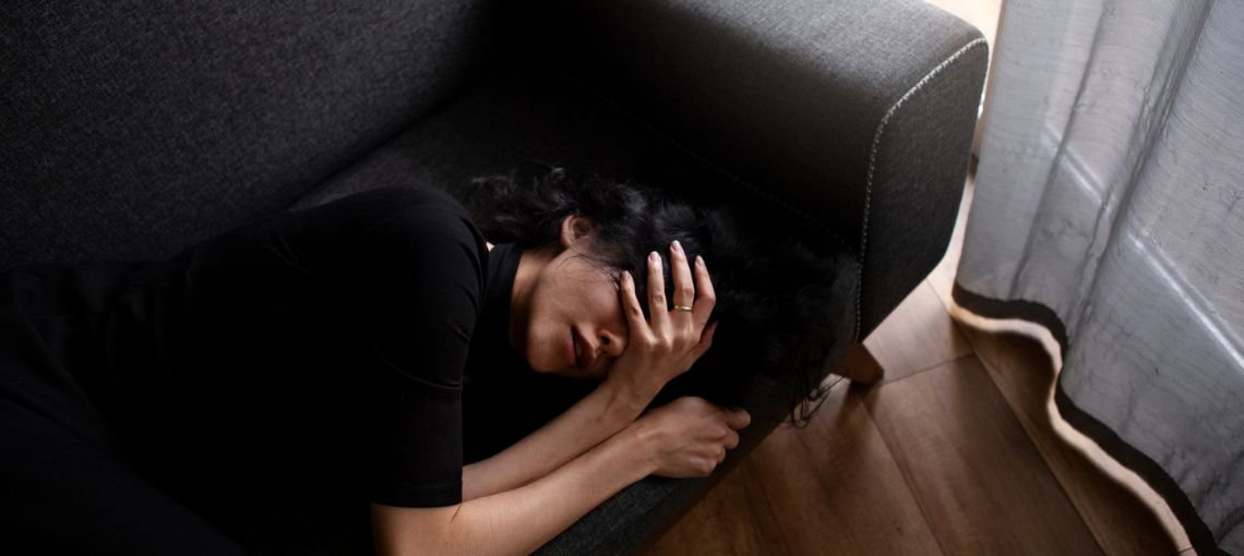 Woman lying on floor beside couch appearing distressed