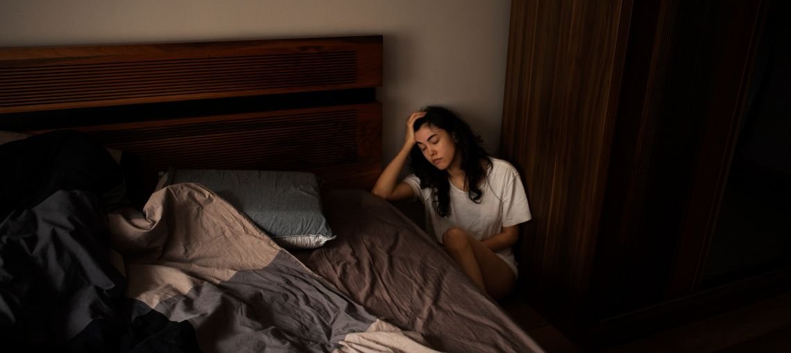 Woman sitting on the bedroom floor holding her head, reflecting emotional distress during trauma recovery