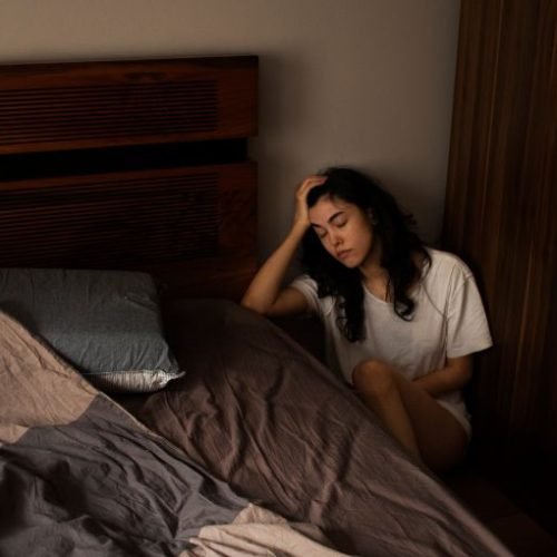 Woman sitting on the bedroom floor holding her head, reflecting emotional distress during trauma recovery